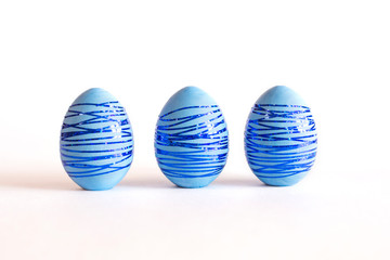 Three blue Easter eggs with blue shiny stripes on a white background.