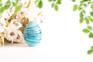Blue Easter egg with blue shiny stripes on a white background. With a green branch in the background.