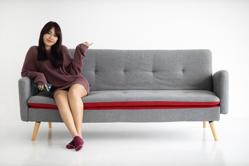 Fototapeta na wymiar Portrait of beautiful young Asian woman is sitting on sofa and pointing finger to empty.