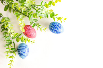 A branch of greenery and Easter eggs on a white background. The view from the top. Flat Easter...