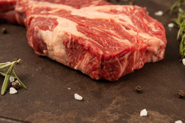 Raw red steak on a cutting board with garlic and rosemary.