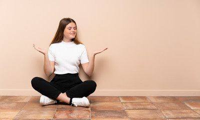 Ukrainian teenager girl sitting on the floor holding copyspace with two hands