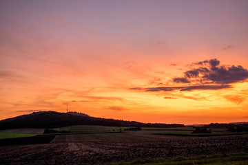 Obraz na płótnie Canvas Sonnenübergang über dem Hesselberg in Mittelfranken (Bayern). Der Himmel leuchtet intensiv und farbenreich in verschiedenen Orangetönen. 