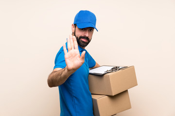 Fototapeta na wymiar Delivery man with beard over isolated background making stop gesture and disappointed