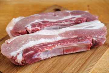 Two pieces of raw pork belly closeup on a wooden table and cutting board.