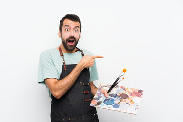 Young artist man holding a palette over isolated background surprised and pointing finger to the...