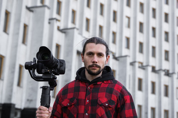 Young Professional videographer holding professional camera on 3-axis gimbal stabilizer. Pro equipment helps to make high quality video without shaking. Cameraman wearing red shirt making a videos.