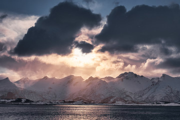 Sunset in cloudy on snowy mountain range in Senja island