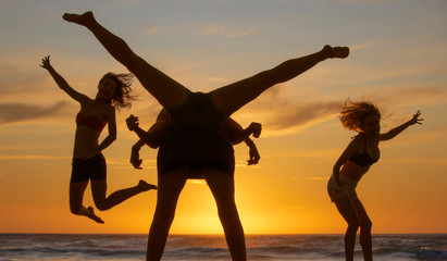 Obraz na płótnie Canvas Silhouette of four beautiful women having fun creating shapes at sunset or sunrise on a beach.