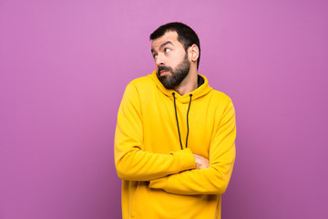 Handsome man with yellow sweatshirt making doubts gesture while lifting the shoulders