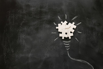 Education concept image. Creative idea and innovation. Puzzle as light bulb metaphor over blackboard