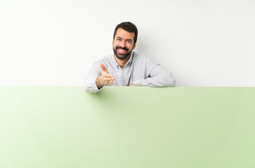 Young handsome man with beard holding a big green empty placard shaking hands for closing a good deal