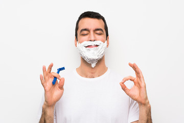 Man shaving his beard over isolated white background in zen pose