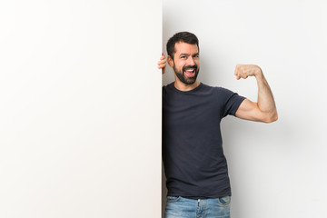 Young handsome man with beard holding a big empty placard doing strong gesture