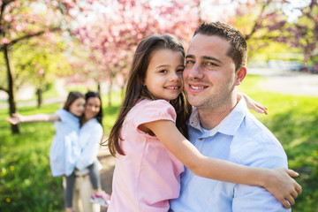 Young parents with small daughters standing outside in spring nature.