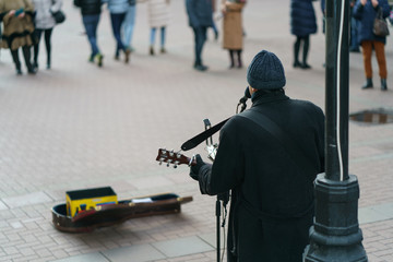 Photography of a street musician plays the guitar on a city street on a spring day.  There is on...