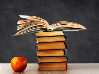 Back to school, pile of books and red apple with empty school board background, education concept.