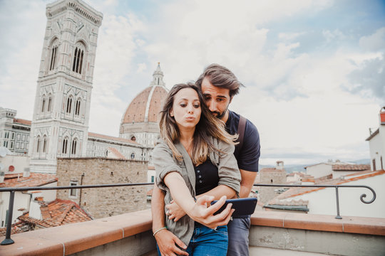 Young couple in love is taking a selfie with the smart phone on a terrace in front of the Florence Cathedral, Church of Santa Maria del Fiore - Millennial having fun together