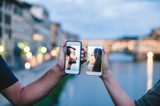 Young loving couple kissing virtually with the smart phone in front of Ponte Vecchio in Florence - Photo of millennials in two phones
