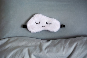 White cute sleep mask made of fluffy faux fur in a cloud shape with closed eyes embroidered on it...