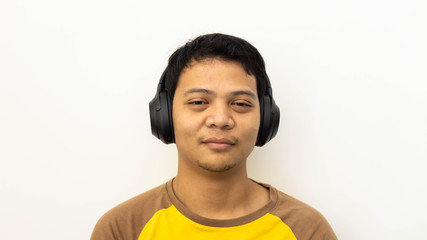 Close-up portrait of happy Asian man smiling while listening to music in headphones with white isolated background.