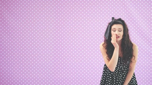 Adorable young girl in black polka-dots dress, leaning to the camera, whispering, waving comically her hands, making faces.