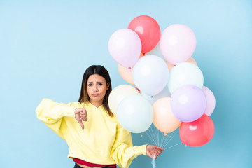 Woman holding balloons in a party over isolated blue background showing thumb down sign
