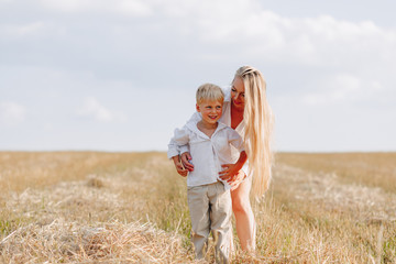 blond little boy playing with mom with white hair with hay in field. summer, sunny weather, farming. happy childhood.