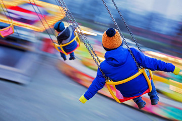 Child, cute boy riding chain swing carousel on sunset, motion blur