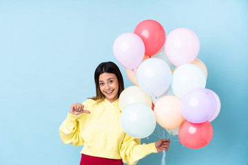 Fototapeta na wymiar Woman holding balloons in a party over isolated blue background proud and self-satisfied