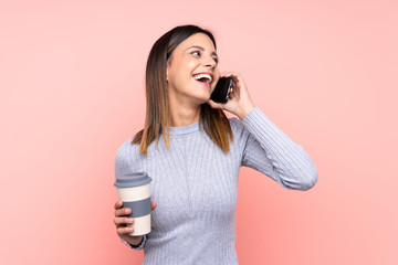 Woman over isolated pink background holding coffee to take away and a mobile