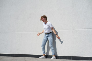 Shorthair redhair girl listening to music in smartphone and singing, standing in front of white wall outdors in summer