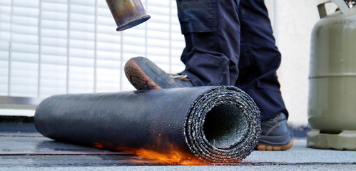 Heating and melting bitumen roofing felt. Flat roof installation with propane blowtorch during...