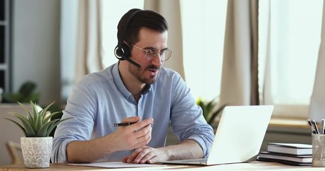 Smiling businessman wear wireless headset making conference video call on laptop. Male professional call center agent, hr manager having distance webcam chat job interview on computer in office. - Powered by Adobe