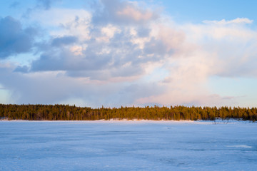 Dramatic sky above the snow-covered frozen Kuito lake, coniferous forest in the background. Winter...