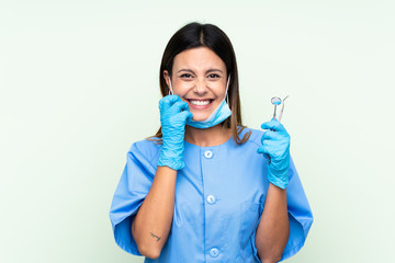 Woman dentist holding tools over isolated green background nervous and scared