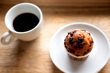 Coffee in white cup and cupcake in white plate on a wooden table for breakfast in the morning