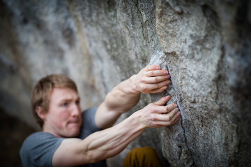 A rock climber climbing on a boulder rock outdoors. Group of friends involved in sports outside.