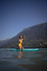 Fototapeta na wymiar Pretty, young woman paddling on a paddle board on a lake, enjoying a lovely summer day