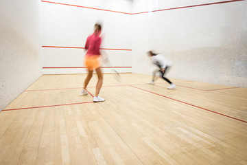 Two female squash players in action on a squash court (motion blurred image; color toned image)