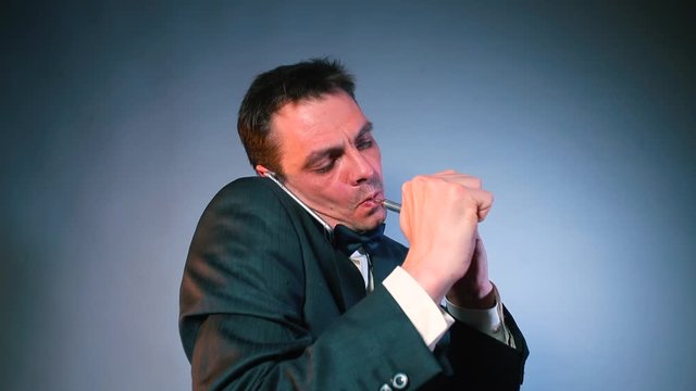 A man in a black suit is talking on the phone and smoking a cannabis pipe. Gray background. The concept of legal use of marijuana.