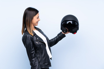 Young brunette woman holding a motorcycle helmet over isolated blue background with happy expression