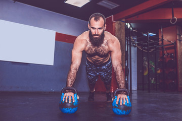 Bearded man doing push ups with kettlebell weights in the gym