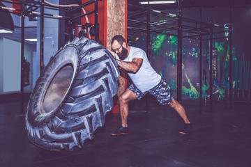 Fototapeta na wymiar Muscular bearded fitness man moving large tire in the crossfit gym