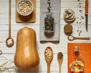 flatlay with pumpkin lagenaria, wooden spoons, different pumpkin seeds, napkins and a glass jar with oil