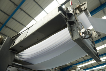 A toilet paper making machine producing toilet and bathroom paper rolls. Paper and tissue manufacturers factory and engineered machinery. Mass produced bathroom products.