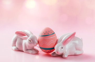 Colored decorated egg and porcelain bunnies on pink background. Easter concept, card with free copy space.