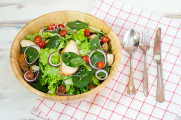 Fresh chicken vegetable salad with fresh tomato, cucumber, lettuce, onion, spinach, sesame, cheese on plate with spoon, fork and knife. Healty food concept