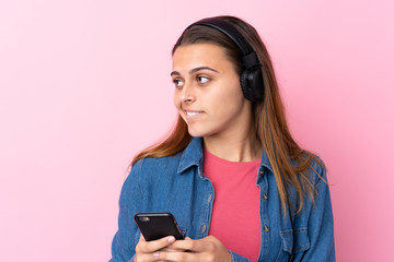 Teenager girl listening music with a mobile over isolated pink wall