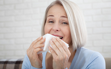 Healthcare, cold, allergy and people concept, sick woman blowing her runny nose in paper tissue on...